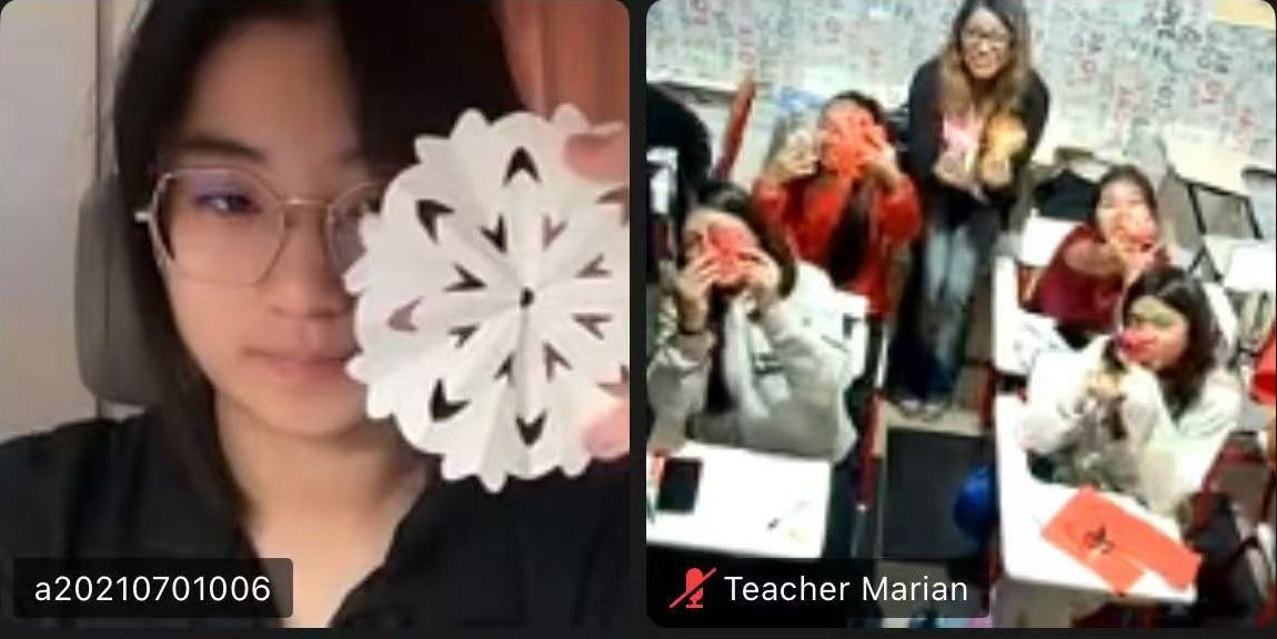 A student holding up a paper cutting next to a classroom of students holding their red paper cuttings